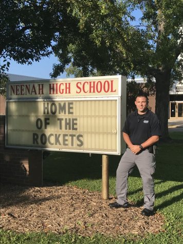 School Resource Officer Nathan Franzke in front of the sign outside of Pickard Auditorium at Neenah High School. 